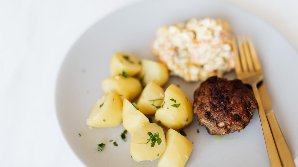 From above of homemade appetizing fried beef cutlet garnished with boiled potatoes with parsley and traditional Russian salad with meat potatoes green peas and mayo placed on plate with cutleries
